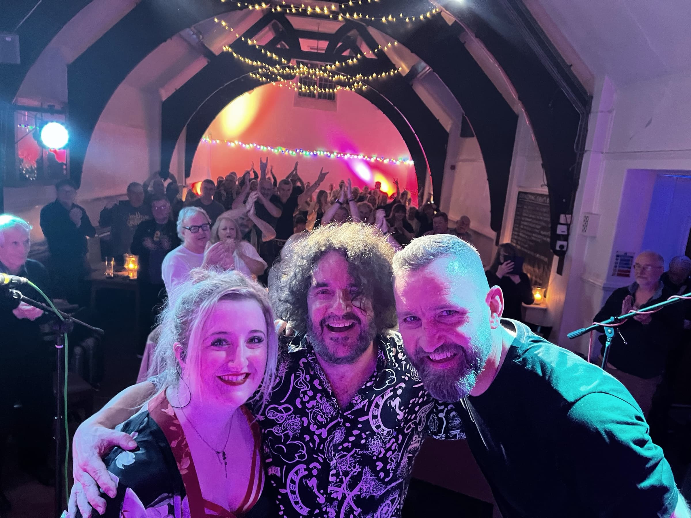 Ian Prowse: three musicians smiling for a selfie in front of the full room