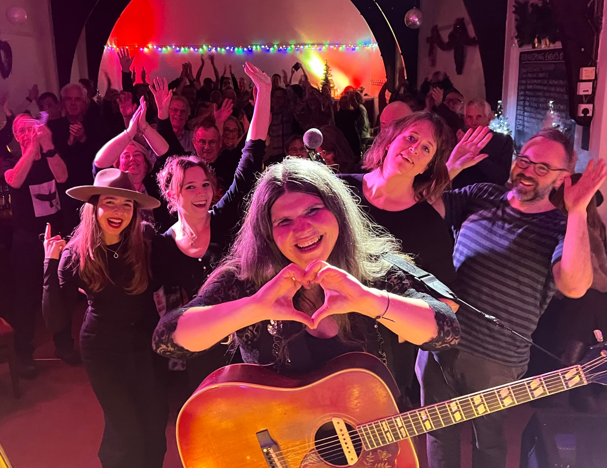 Michele Stodart (The Magic Numbers): a guitarist making a heart with her hands, friends around her and the crowd cheering behind