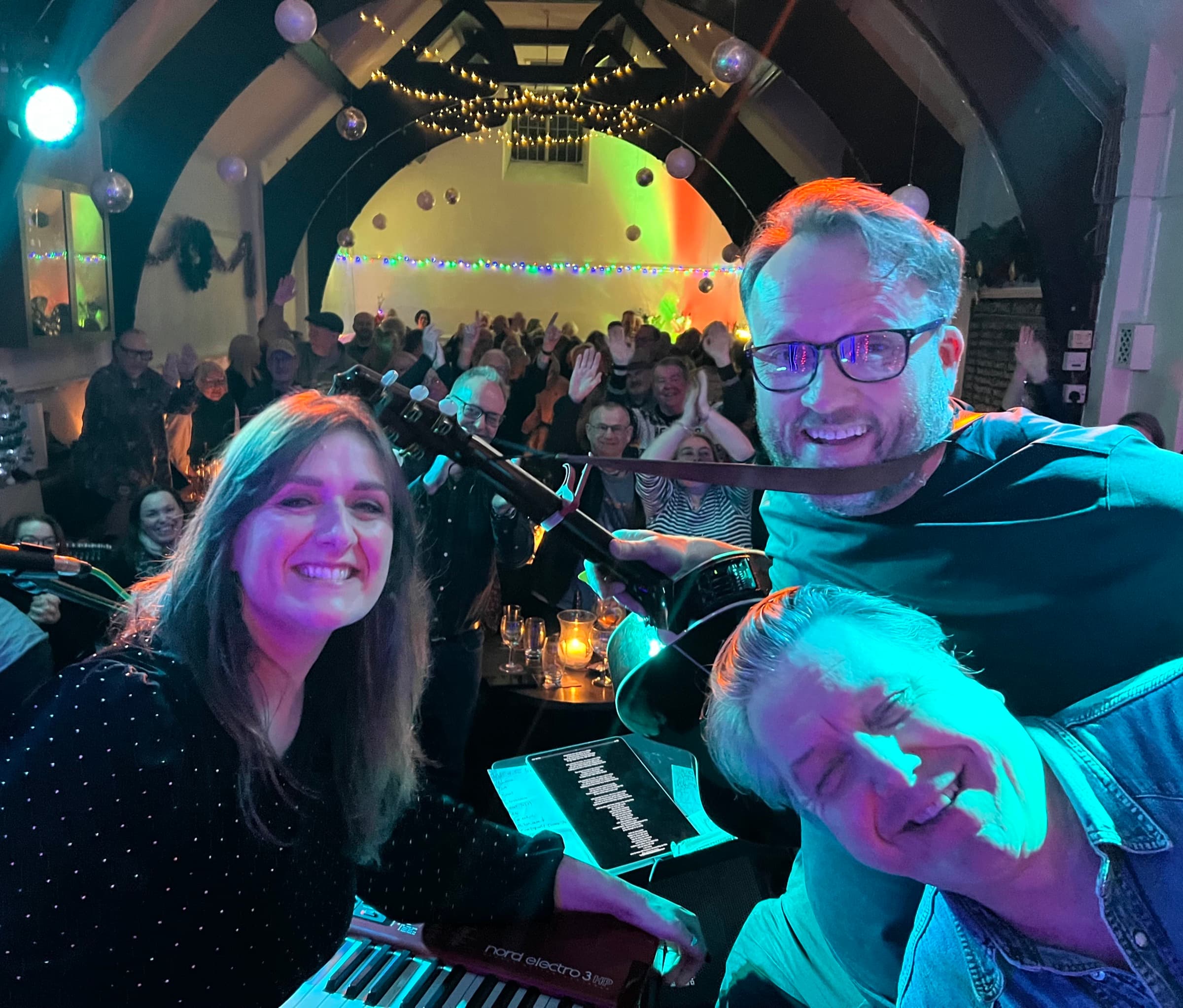 Robert Vincent: three musicians at the keyboard smiling for a selfie, the room full behind them
